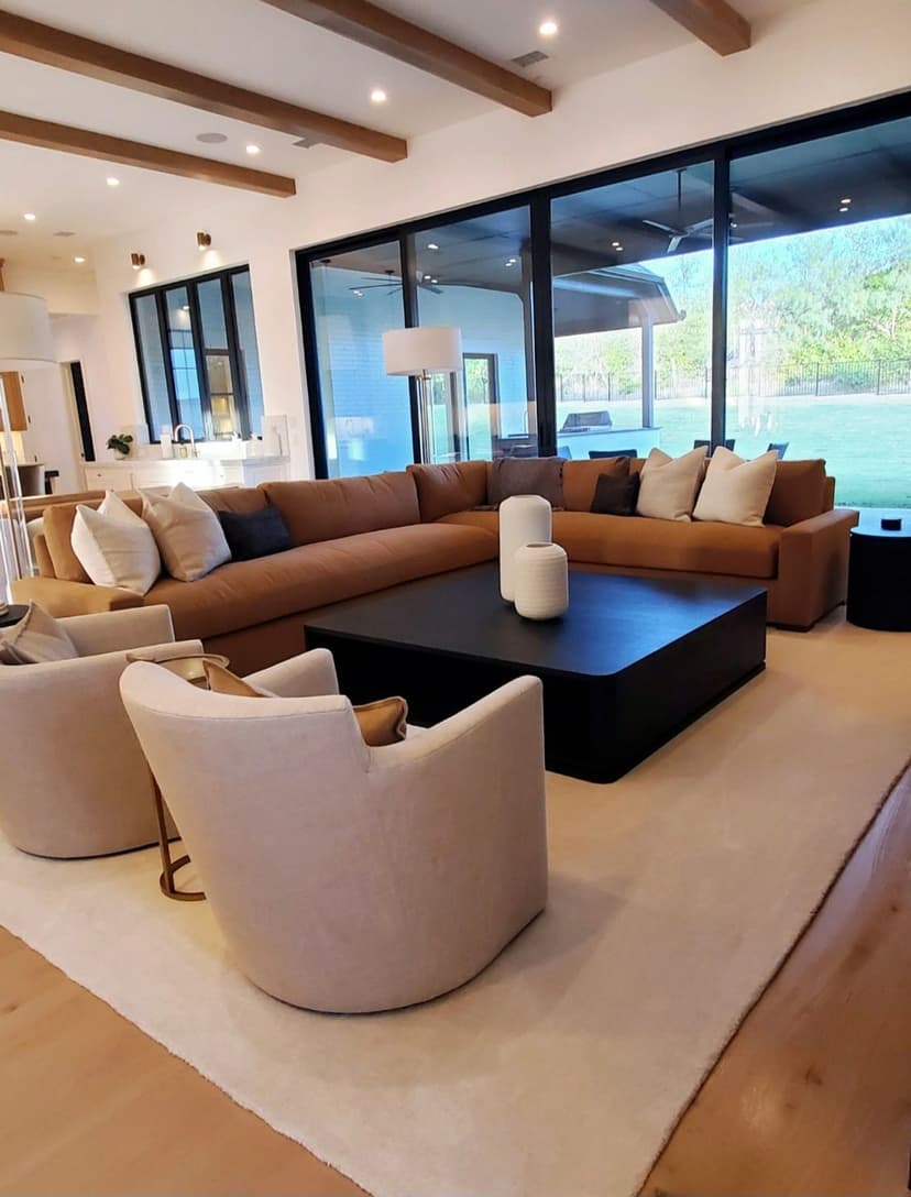 Modern living room with a large sectional sofa, round chairs, and large windows showcasing greenery.