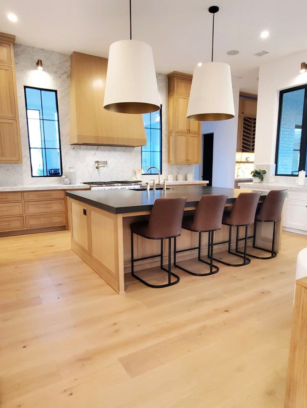 Modern kitchen with wooden cabinets, marble countertops, and stylish bar stools. Spacious design.