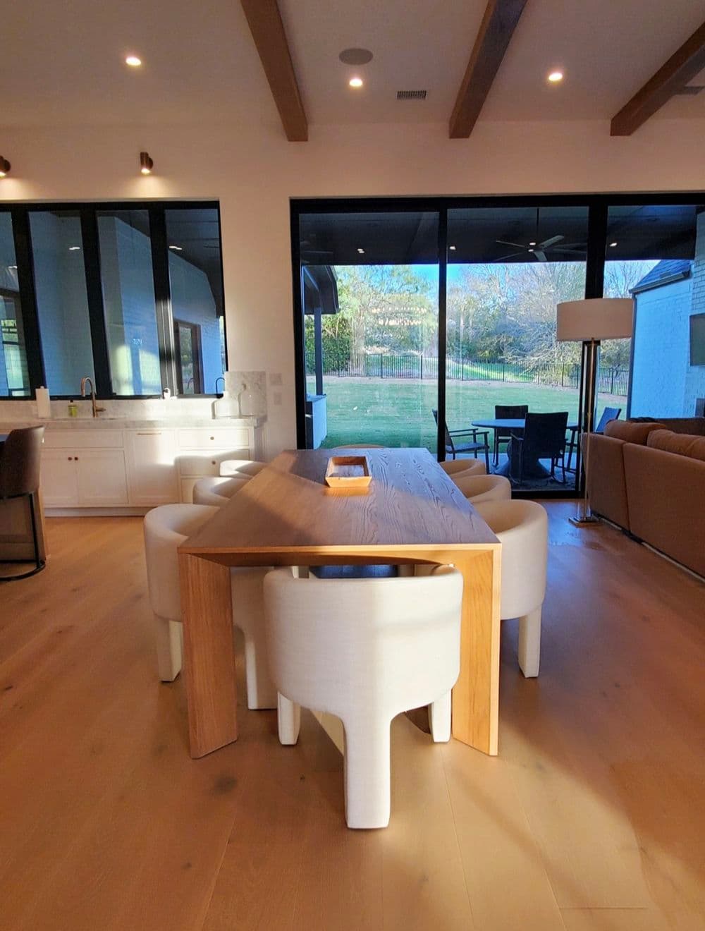Modern dining area featuring a wooden table and white chairs, large windows with outdoor view.