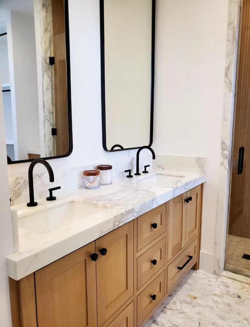 Modern bathroom with dual sinks, black faucets, and wooden cabinetry against a marble countertop.