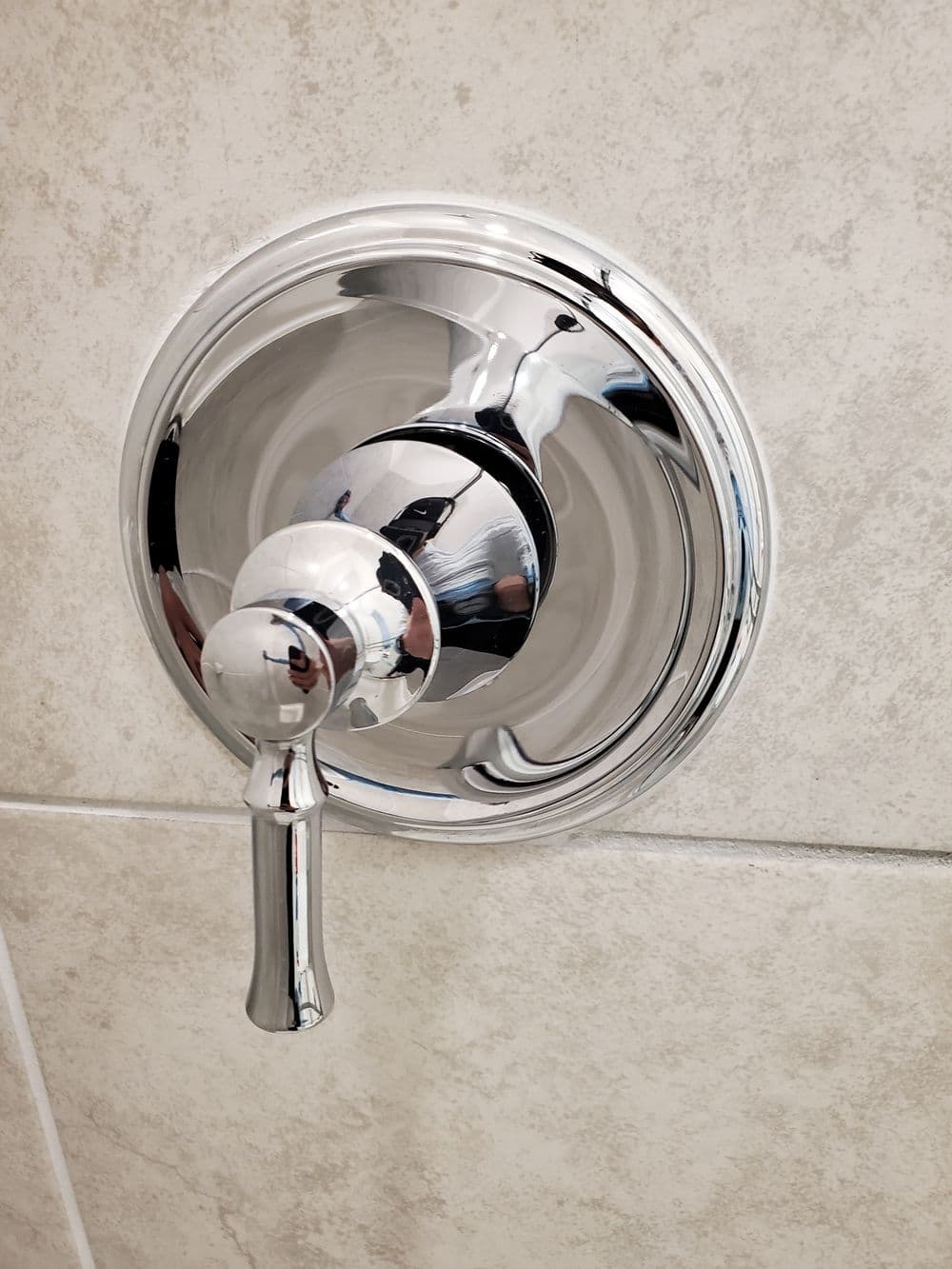 Chrome shower control knob on a textured tile wall, reflecting light.