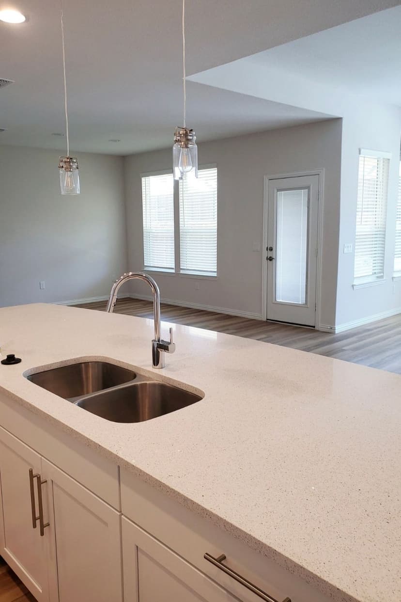 Modern kitchen with white quartz countertop, double sink, and pendant lights overlooking living area.